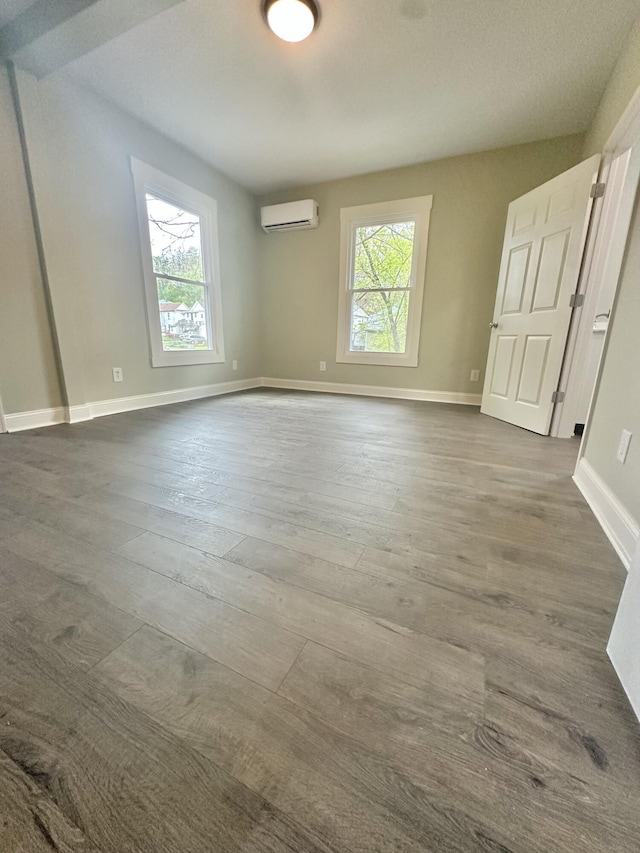 unfurnished bedroom with dark wood finished floors, an AC wall unit, and baseboards