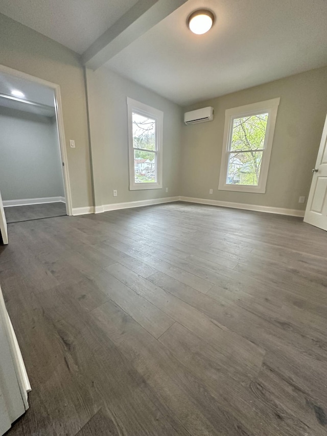 empty room featuring dark wood finished floors, plenty of natural light, an AC wall unit, and baseboards