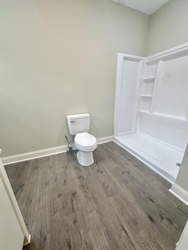 bathroom with baseboards, wood finished floors, a shower stall, and toilet