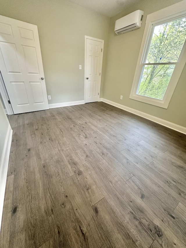 empty room with dark wood finished floors, baseboards, and a wall unit AC