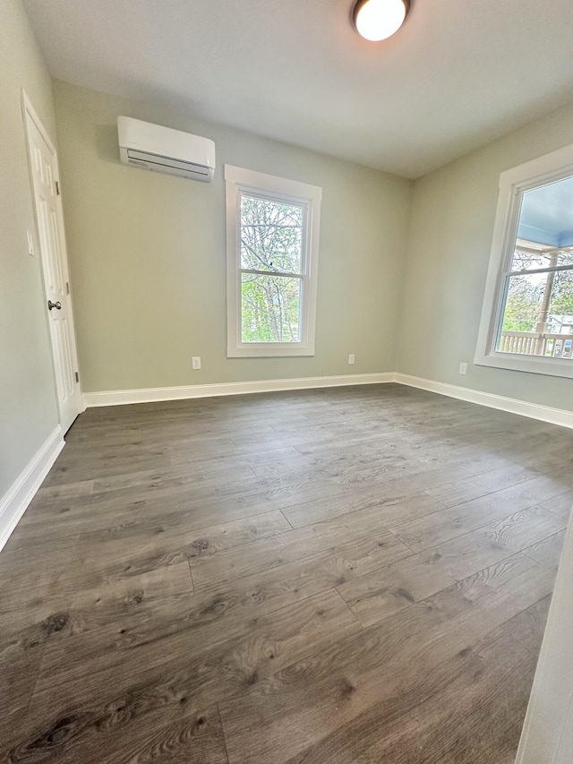 empty room with baseboards, a wall mounted AC, and dark wood-style flooring