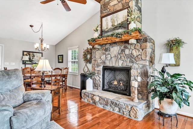 living room with baseboards, high vaulted ceiling, ceiling fan with notable chandelier, wood finished floors, and a fireplace