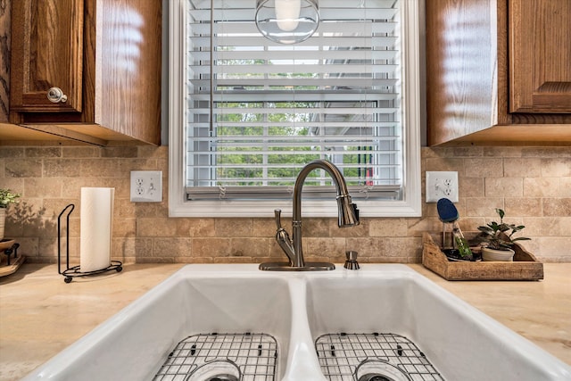 room details featuring brown cabinetry, light countertops, a sink, and tasteful backsplash