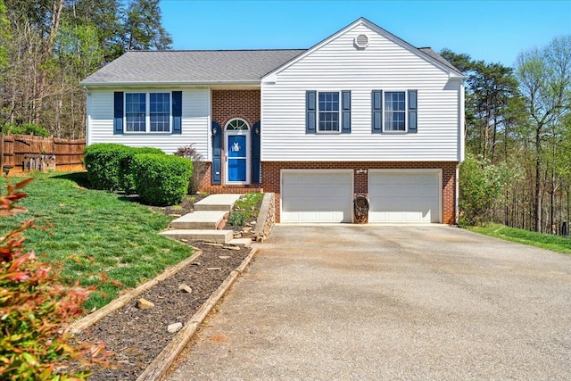 bi-level home with brick siding, an attached garage, fence, and driveway
