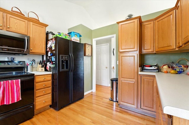 kitchen featuring brown cabinetry, light wood-type flooring, light countertops, and black appliances