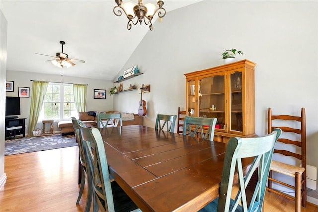 dining space featuring light wood-style floors, ceiling fan with notable chandelier, and high vaulted ceiling