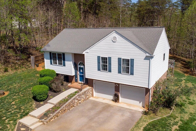 split foyer home featuring a garage, brick siding, driveway, and a forest view
