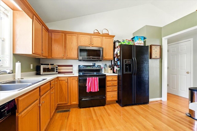 kitchen featuring a sink, light countertops, black appliances, and vaulted ceiling