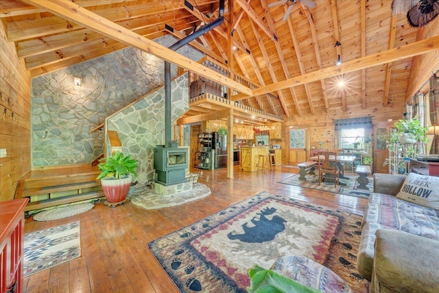living room featuring beamed ceiling, wood ceiling, wooden walls, a wood stove, and wood-type flooring