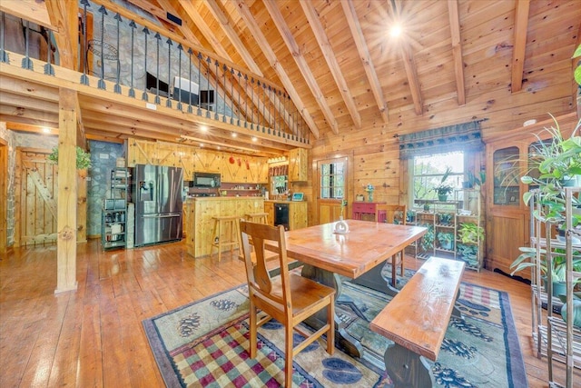 dining area featuring beam ceiling, light wood-style flooring, wood walls, and high vaulted ceiling