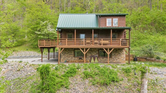 back of house featuring stone siding, a wooded view, log siding, and a deck