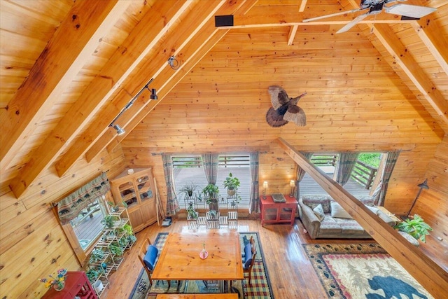 living area with lofted ceiling with beams, wooden ceiling, wood walls, and ceiling fan