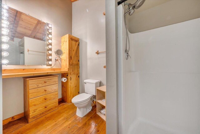 bathroom with hardwood / wood-style floors, vanity, a walk in shower, and toilet