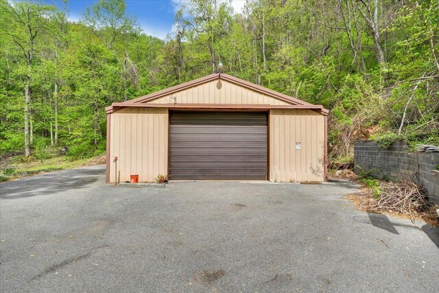 detached garage featuring aphalt driveway and a forest view