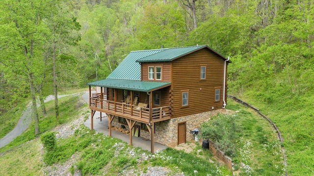 back of property featuring a wooded view, stone siding, metal roof, a wooden deck, and a standing seam roof