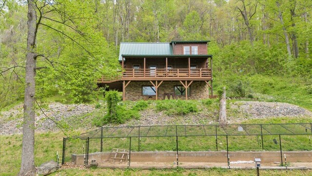 back of property with a wooded view, stone siding, log siding, fence, and metal roof
