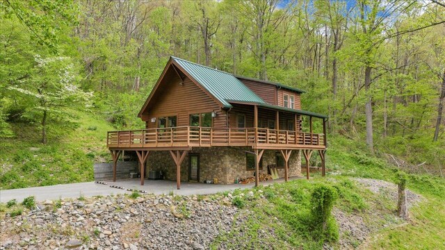 exterior space with stone siding, metal roof, a view of trees, a deck, and a patio