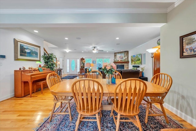 dining area featuring ceiling fan, baseboards, a large fireplace, and light wood-type flooring