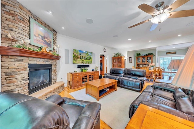 living room featuring light wood-type flooring, ornamental molding, a stone fireplace, and ceiling fan