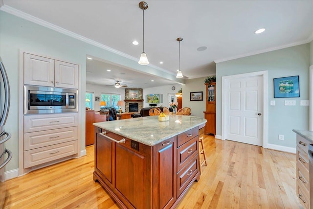 kitchen with light stone counters, light wood-style floors, decorative light fixtures, stainless steel microwave, and ornamental molding