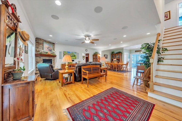 living room featuring light wood-type flooring, ceiling fan, a fireplace, and stairway