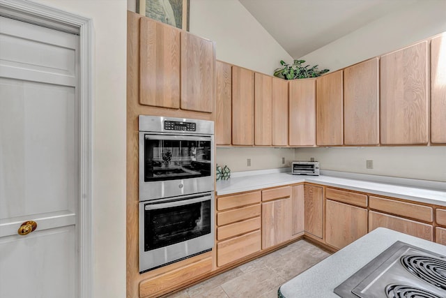 kitchen with double oven, light brown cabinetry, light countertops, vaulted ceiling, and light tile patterned floors