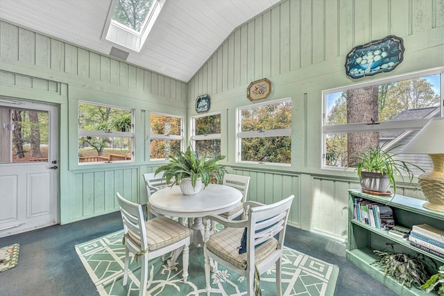 sunroom / solarium featuring vaulted ceiling with skylight, wooden walls, and carpet