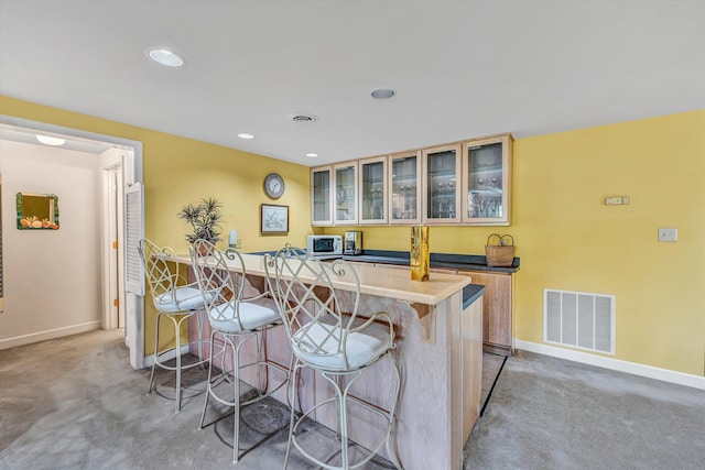 kitchen with a kitchen bar, baseboards, visible vents, and light colored carpet