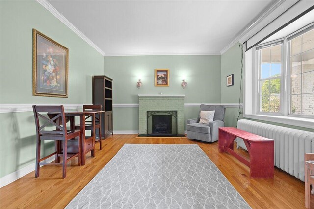 living area with radiator, ornamental molding, wood finished floors, and a brick fireplace