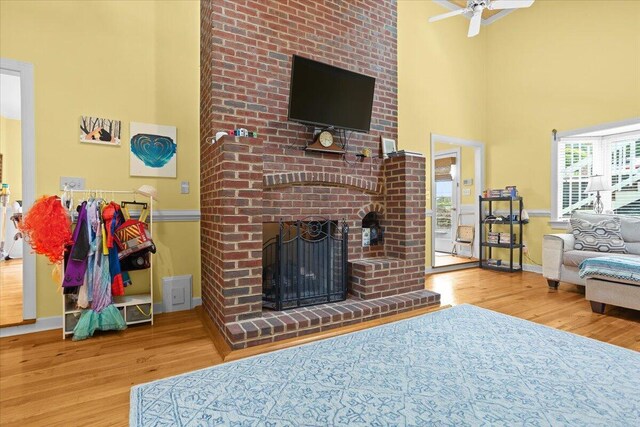 living room featuring wood finished floors, a fireplace, ceiling fan, baseboards, and a high ceiling