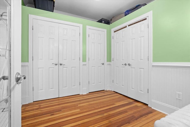 unfurnished bedroom with a wainscoted wall, two closets, and wood finished floors