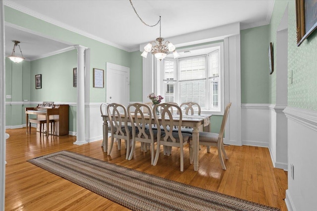 dining room featuring ornate columns, wood finished floors, a chandelier, and ornamental molding
