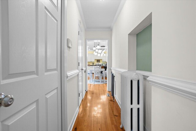 hallway featuring radiator, a chandelier, crown molding, and light wood finished floors