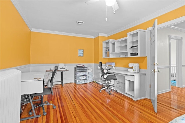 office space with radiator, crown molding, built in study area, wainscoting, and wood finished floors
