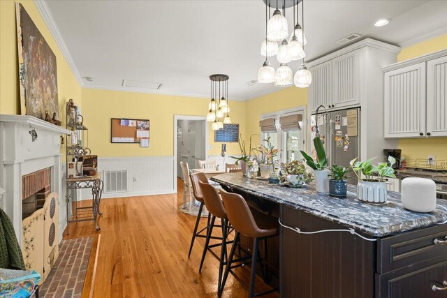 kitchen with ornamental molding, dark stone countertops, wainscoting, a kitchen island, and white cabinetry