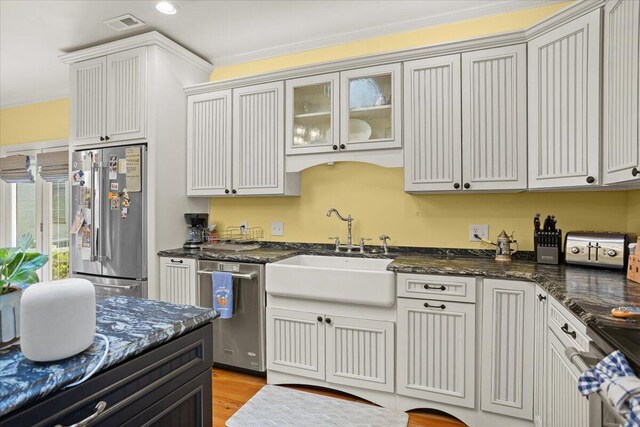 kitchen featuring stainless steel appliances, a sink, ornamental molding, dark stone counters, and light wood-type flooring