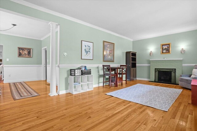 living room with ornate columns, crown molding, wood finished floors, and a brick fireplace