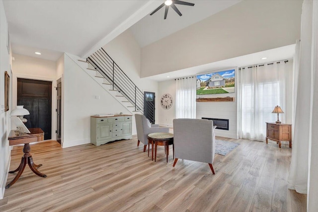 dining space with a large fireplace, light wood-type flooring, baseboards, stairs, and ceiling fan