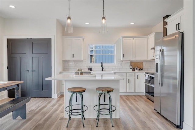kitchen featuring stainless steel appliances, a breakfast bar, light countertops, and white cabinetry