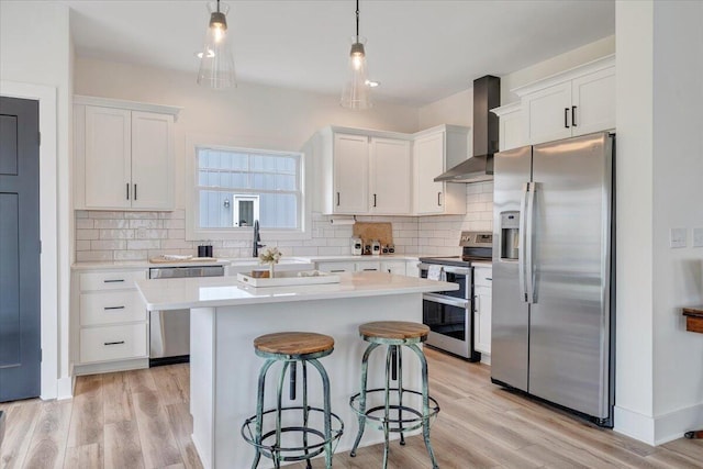 kitchen featuring stainless steel appliances, white cabinets, a breakfast bar area, and wall chimney range hood