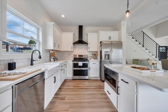 kitchen featuring white cabinetry, backsplash, wall chimney exhaust hood, appliances with stainless steel finishes, and a sink