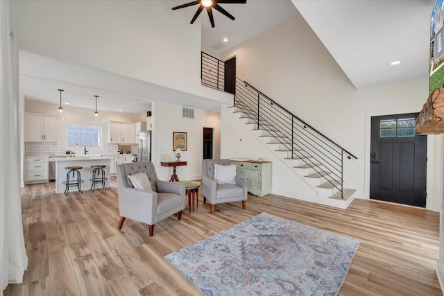foyer entrance with light wood-type flooring, stairway, a high ceiling, a ceiling fan, and visible vents