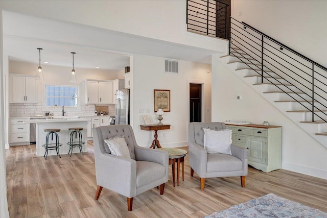 living room featuring light wood-style floors, stairway, visible vents, and baseboards