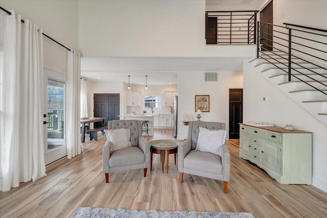 living area with plenty of natural light, a towering ceiling, visible vents, and light wood finished floors