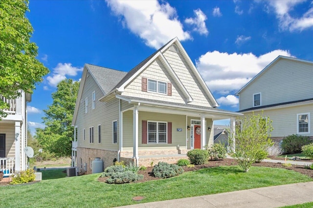 bungalow-style house with central air condition unit, a front lawn, a shingled roof, covered porch, and brick siding