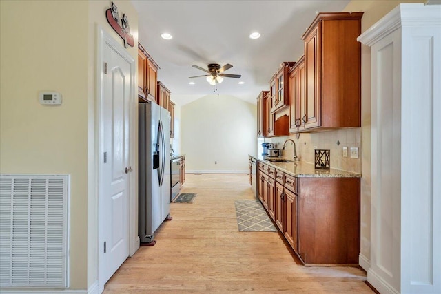 kitchen with a sink, ceiling fan, light wood finished floors, stainless steel refrigerator with ice dispenser, and visible vents