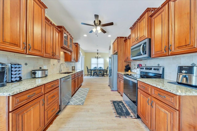 kitchen with stainless steel appliances, a sink, light wood-type flooring, brown cabinetry, and ceiling fan with notable chandelier