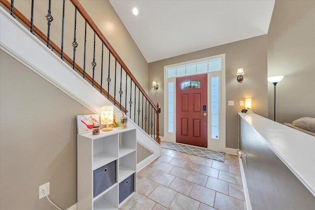 foyer featuring lofted ceiling, baseboards, stairs, and light tile patterned flooring