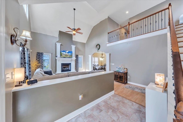 living area with baseboards, high vaulted ceiling, stairway, ceiling fan, and a fireplace