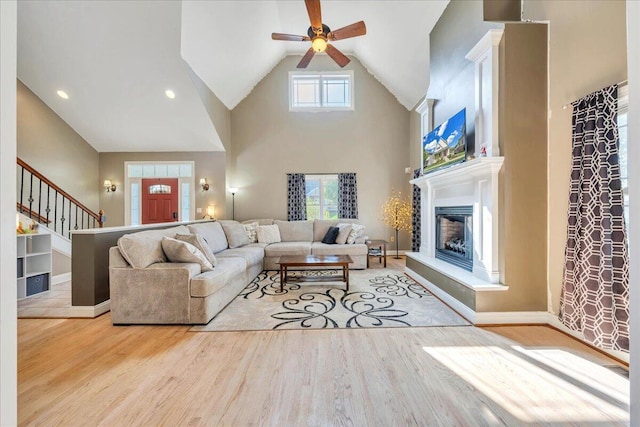 living room featuring a glass covered fireplace, wood finished floors, a ceiling fan, and high vaulted ceiling